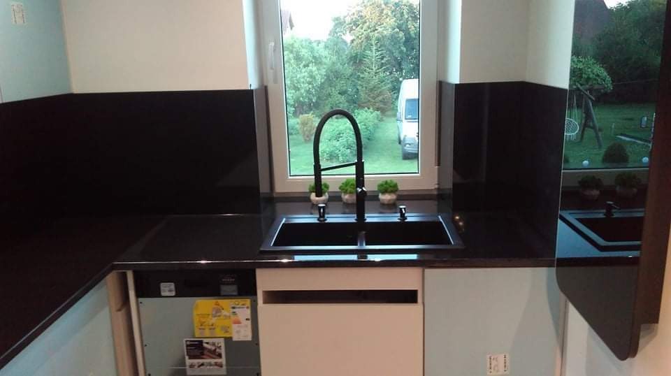 Nowoczesna kuchnia z czarnym blatem i zlewozmywakiem, minimalistyczna armatura, okno z widokiem na zieleń, dekoracyjne rośliny w doniczkach.