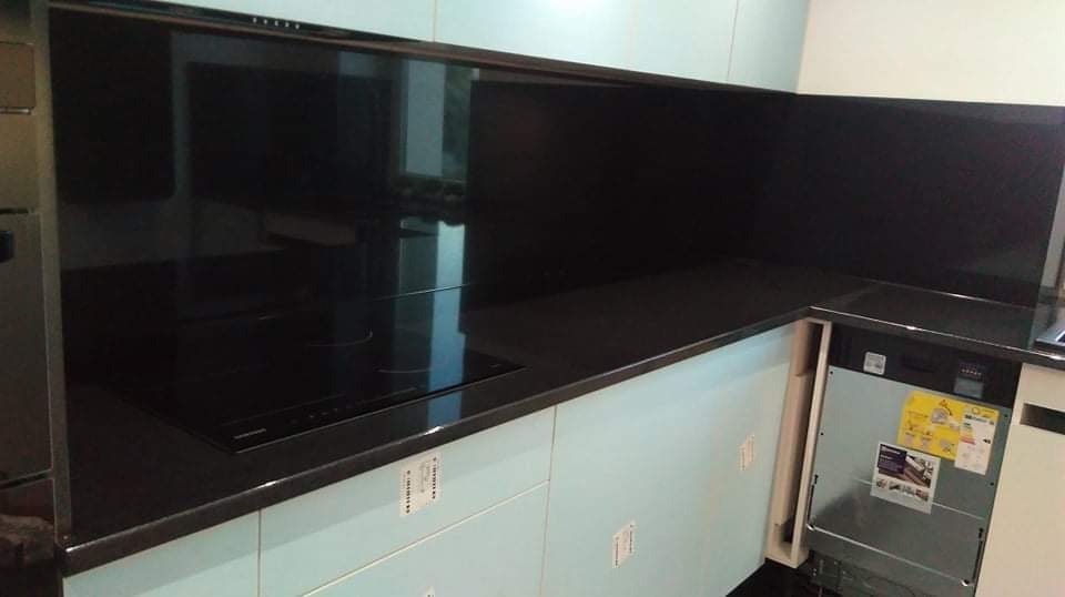 Nowoczesna kuchnia z czarnym szklanym panelem nad blatem i płytą indukcyjną, jasnoniebieskie szafki, widoczna z boku zabudowana zmywarka.