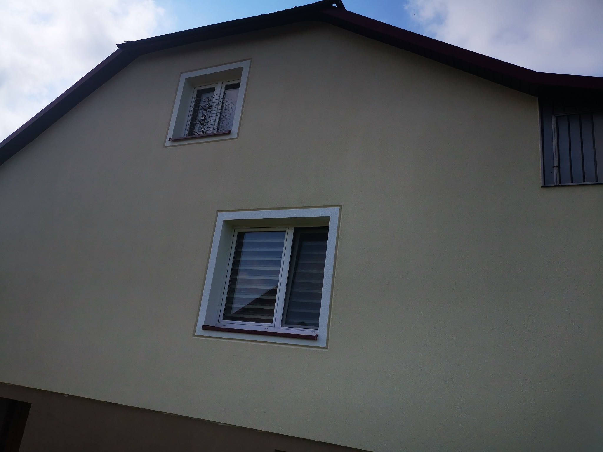 Fragment ocieplonej elewacji budynku w Jarosławiu z dwoma oknami PCV, jedno z roletami poziomymi, drugie z kratą zabezpieczającą.