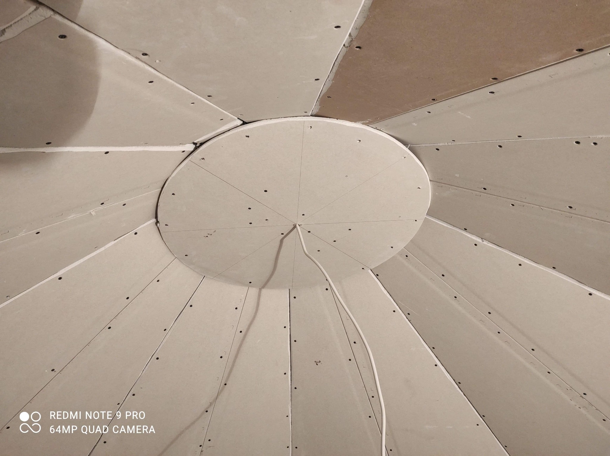 Sufit z płyty kartonowo-gipsowej w trakcie montażu, widoczne łączenia płyt i przewód elektryczny wychodzący z centralnej okrągłej części.