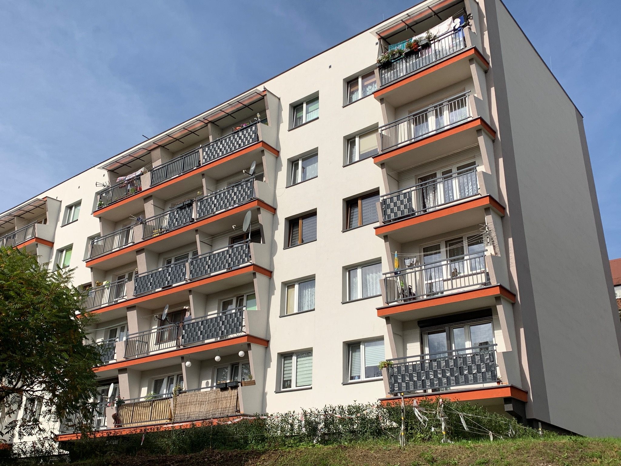 Wielopiętrowy budynek mieszkalny z balkonami o szarych, metalowych balustradach z pomarańczowymi akcentami, widok z dołu pod kątem.