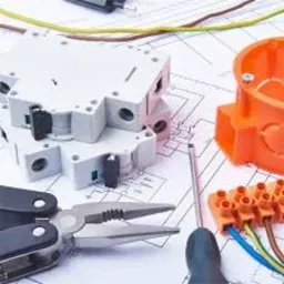 Szczegółowe ujęcie elementów instalacji elektrycznej: bezpieczniki, puszka instalacyjna, listwa zaciskowa z podłączonymi przewodami, multitoolem i śrubokrętem na tle schematu elektrycznego.