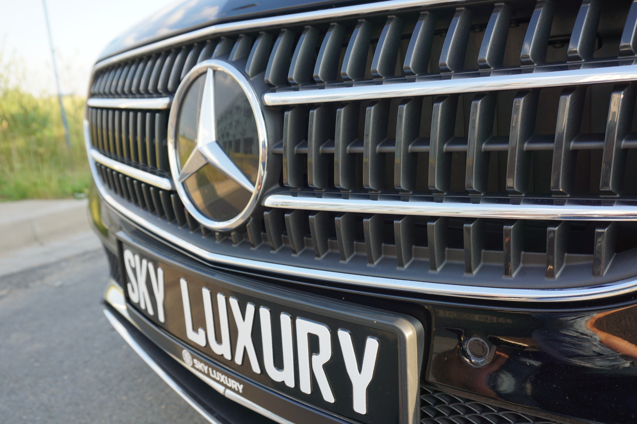 Czarny samochód marki Mercedes z chromowanym grillem i logo, tablica rejestracyjna z napisem 'SKY LUXURY'.