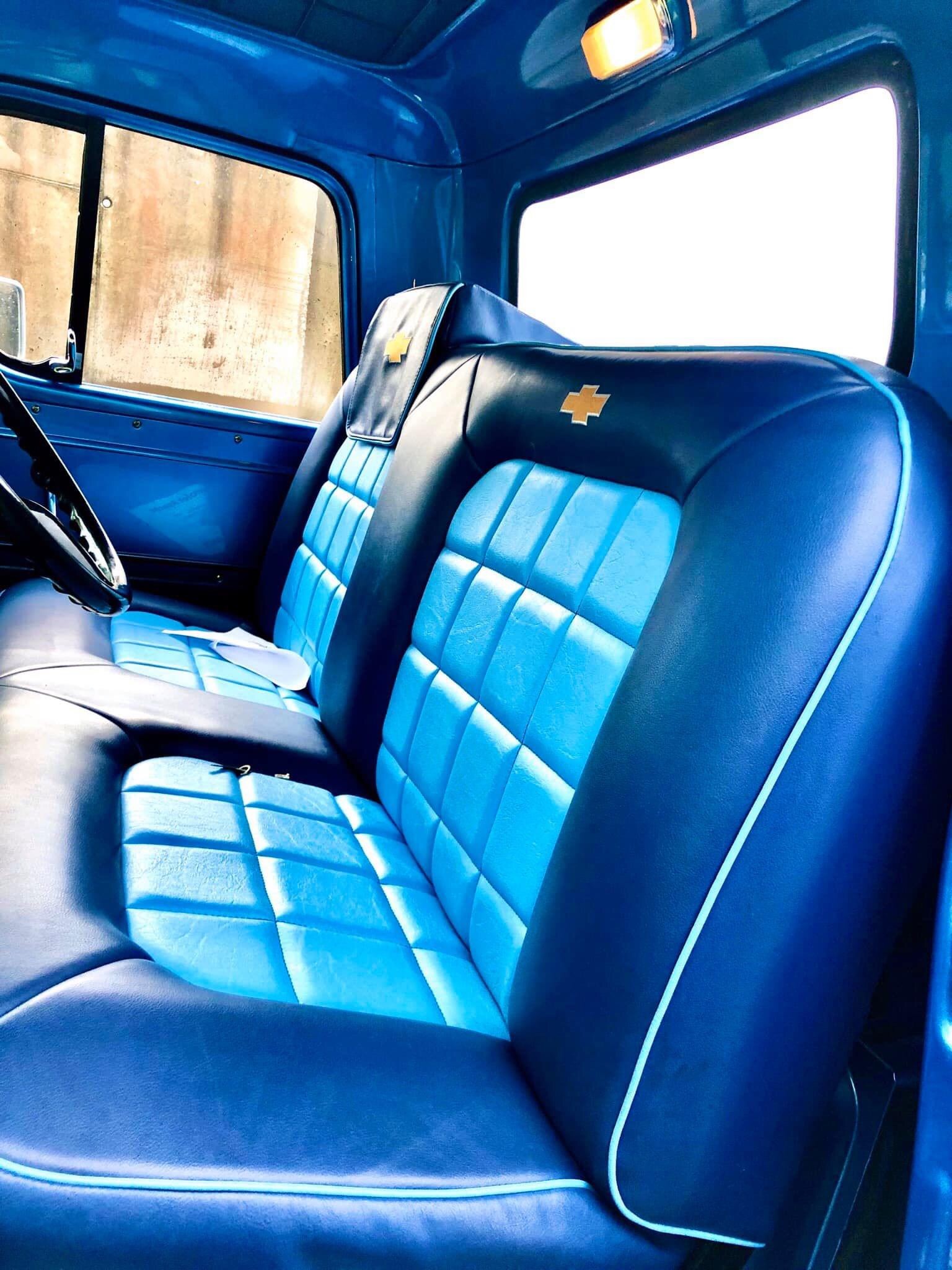 Wnętrze odrestaurowanego samochodu: dwukolorowe, niebieskie fotele z pikowaniem w romby, ozdobione logo, widoczne fragmenty deski rozdzielczej i kierownicy.