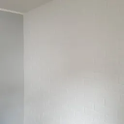 Świeżo pomalowana na biało ściana z efektem cegieł w Radziejowie, z szarą ścianą boczną i listwą przypodłogową, widoczne niedoskonałości faktury.