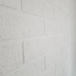 Biała ściana z cegieł pomalowana na biało, widoczna z boku, z lekką teksturą i nierównościami.