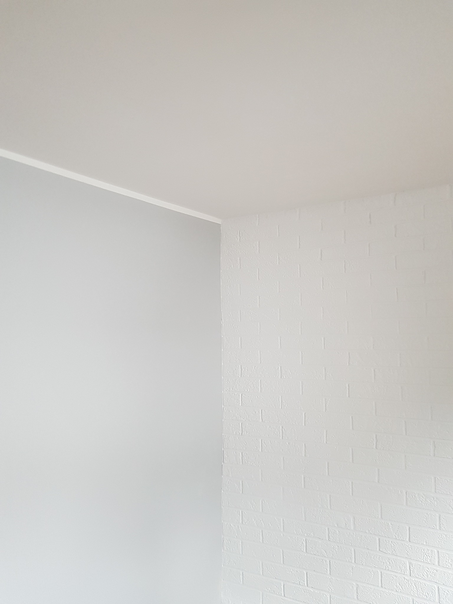 Świeżo pomalowany narożnik pokoju z jedną ścianą w odcieniu szarości i drugą w bieli imitującą cegłę.