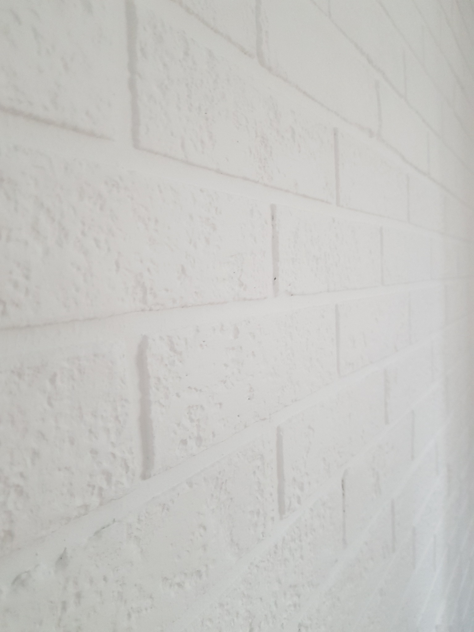 Biała ściana z cegieł pomalowana na biało, widoczna z boku, z lekką teksturą i nierównościami.