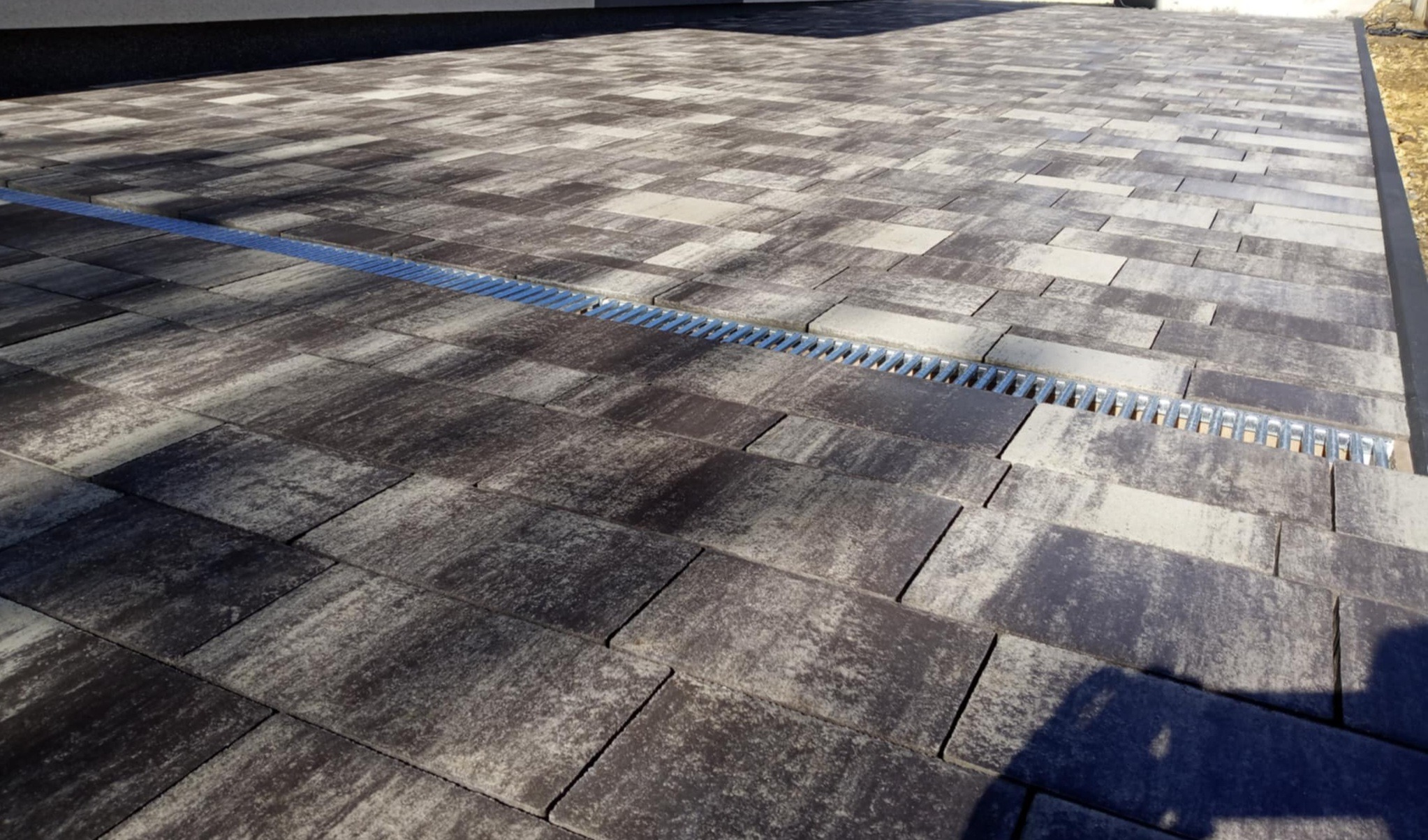 Ułożona, szara kostka brukowa z odpływem liniowym. Nowoczesna nawierzchnia z widoczną strukturą kamienia i srebrnym odpływem wzdłuż krawędzi.