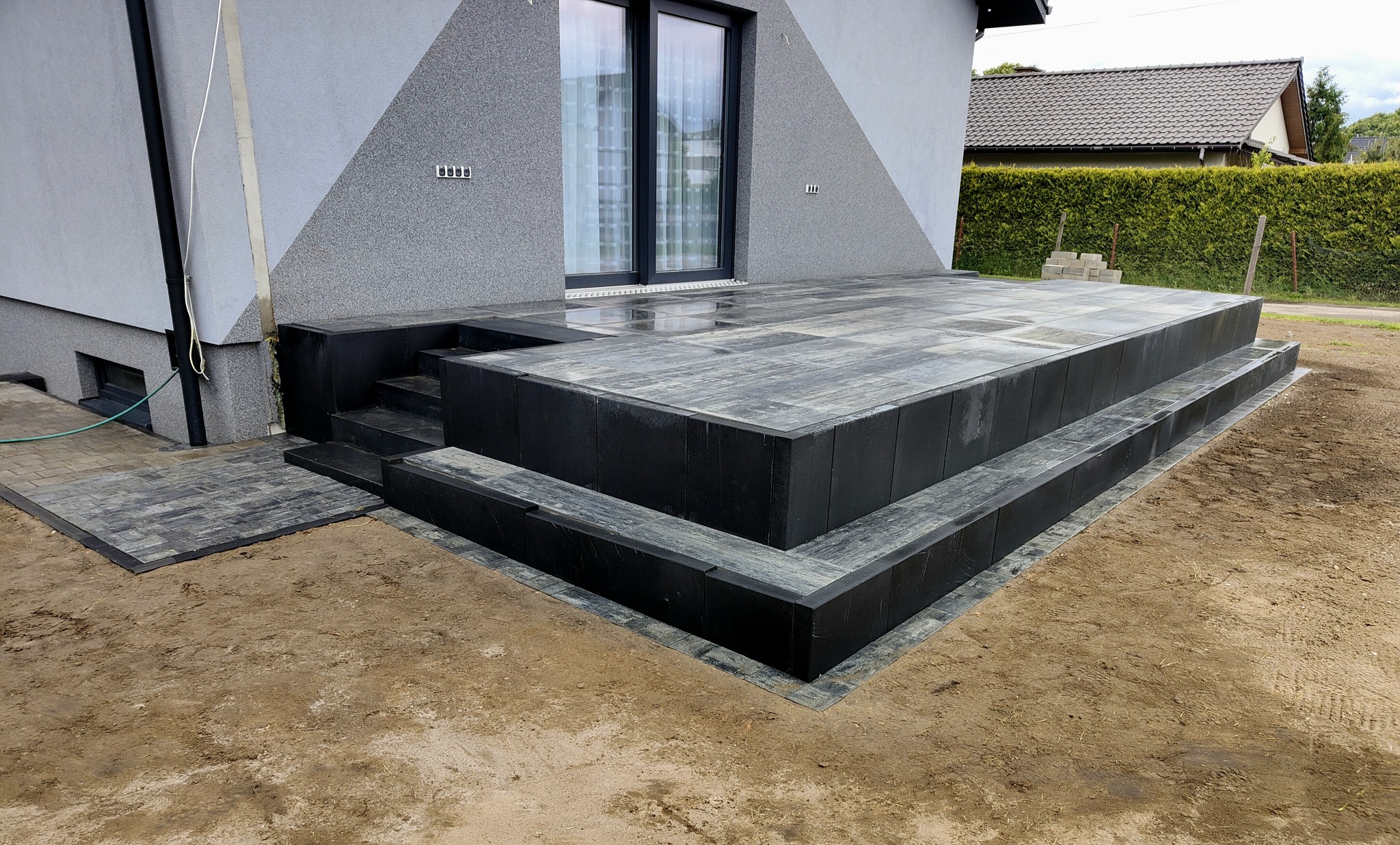 Nowoczesny taras z kostki brukowej w Strzyżowicach, z wyraźnymi schodami i precyzyjnym wykończeniem. Szaro-czarna kolorystyka, minimalistyczny design.