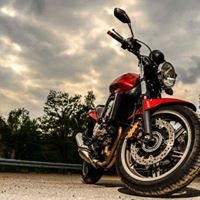 Czerwony motocykl typu cruiser zaparkowany na poboczu drogi, z widocznymi drzewami w tle i pochmurnym niebem