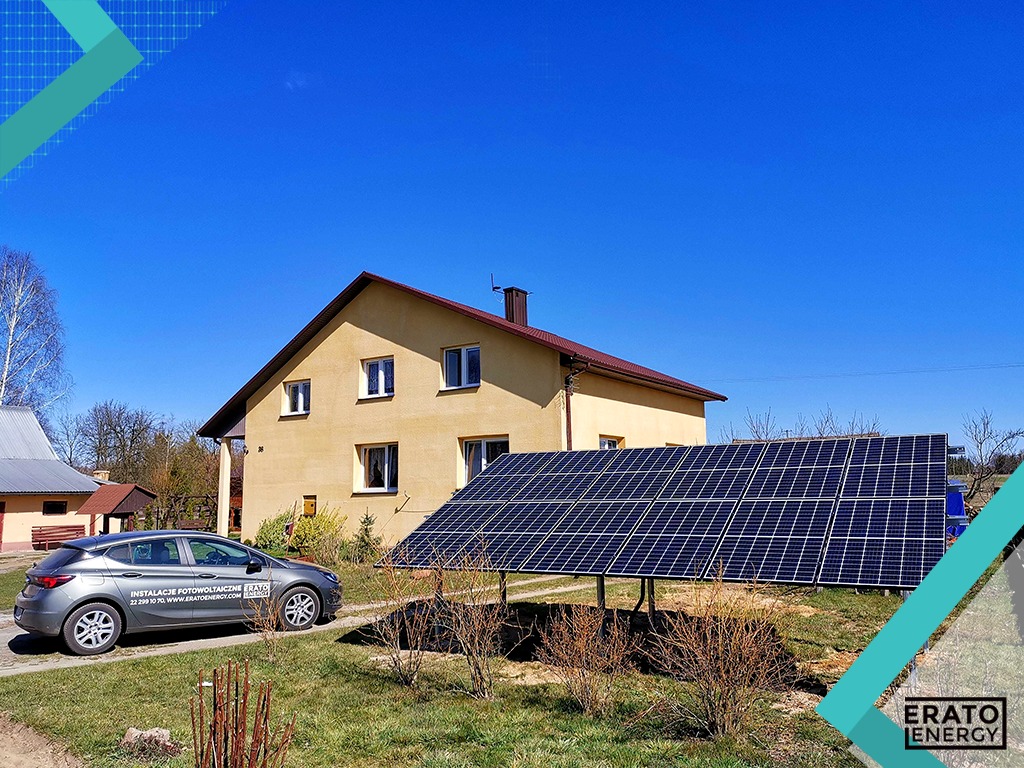 Instalacja paneli słonecznych na gruncie przed domem jednorodzinnym, szary samochód z logo firmy instalacyjnej zaparkowany obok.