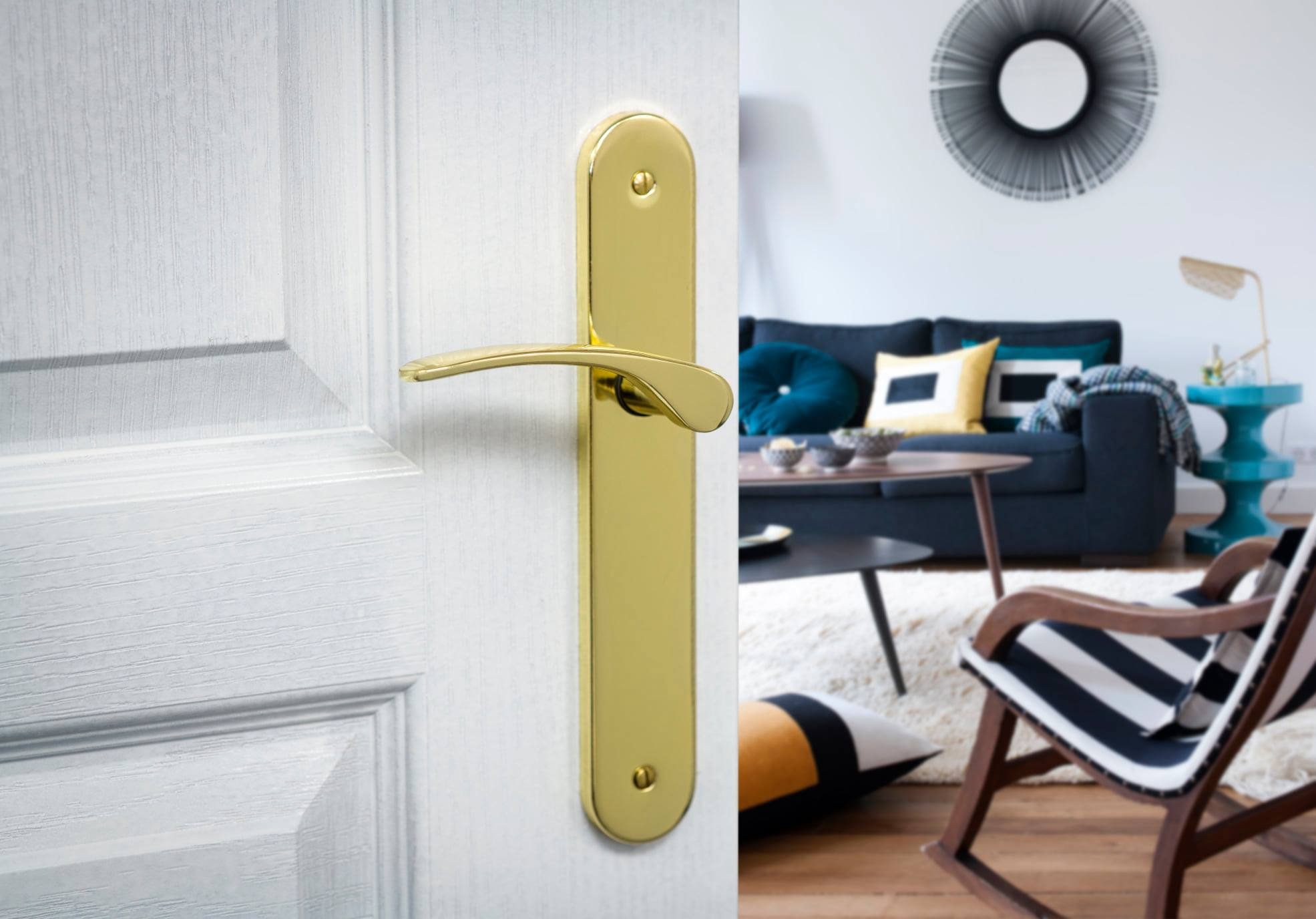 Złota klamka na białych drzwiach z widocznym fragmentem salonu w tle.