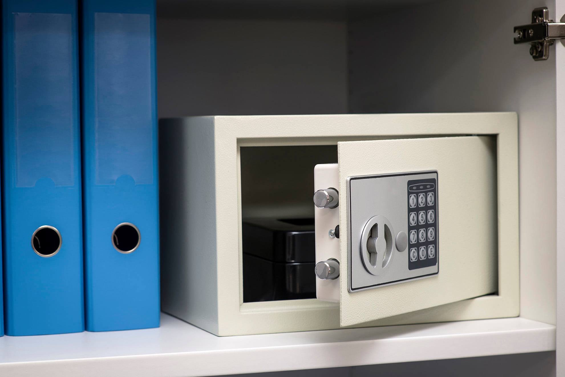 Otwarty sejf z elektronicznym zamkiem, umieszczony na półce w szafie obok dwóch niebieskich segregatorów.
