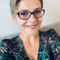 Portret uśmiechniętej kobiety w okularach i kwiecistej sukience, potencjalnej specjalistki od finansów w Krakowie.