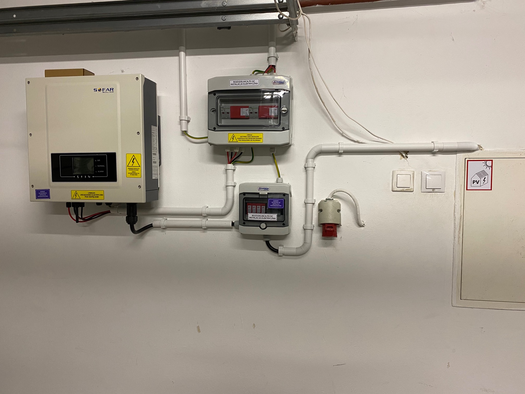 Zamontowany inwerter Sofar Solar z rozdzielnicami AC i DC na białej ścianie, widoczne przewody i oznaczenia ostrzegawcze.