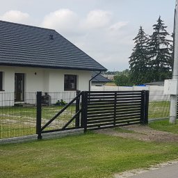 Mobilne Usługi Stolarsko - Spawalnicze Sylwester Kostecki - Nowoczesne ogrodzenie panelowe z bramą przesuwną w kolorze czarnym, na tle domu z ciemną dachówką i zieleni drzew.