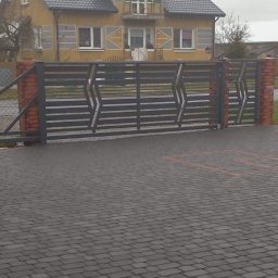 Mobilne Usługi Stolarsko - Spawalnicze Sylwester Kostecki - Przesuwna brama panelowa z poziomymi szczeblami i ceglanymi słupkami na posesji z kostki brukowej, w tle widoczny dom.