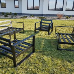 Mobilne Usługi Stolarsko - Spawalnicze Sylwester Kostecki - Cztery czarne, metalowe krzesła ogrodowe ustawione na trawniku przed nowoczesnym domem z białymi ścianami i ciemnymi oknami.