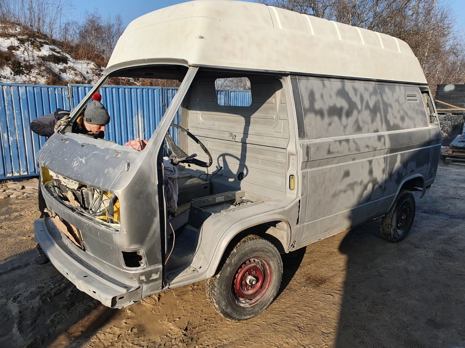 Przygotowanie do lakierowania: szlifowanie karoserii zdekompletowanego busa VW T3 z wysokim dachem, widoczny pracownik w czapce i rękawicach, brak elementów wyposażenia, wstępna warstwa podkładu...