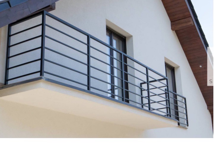 Czarna, metalowa balustrada balkonowa z poziomymi szczeblami, zamontowana na jasnym balkonie domu jednorodzinnego z brązowymi oknami i drewnianym podbitką dachu.