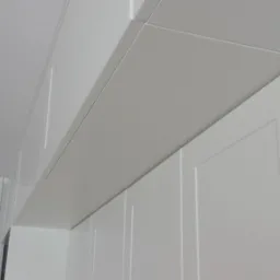 Białe, modułowe szafki kuchenne pod sufitem z widocznym kablem i żarówką w tle, ukazujące detale wykończenia i montażu.