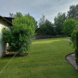 Nawadnianie trawnika z rolki przy ścianie budynku, widoczny fragment systemu nawadniania.