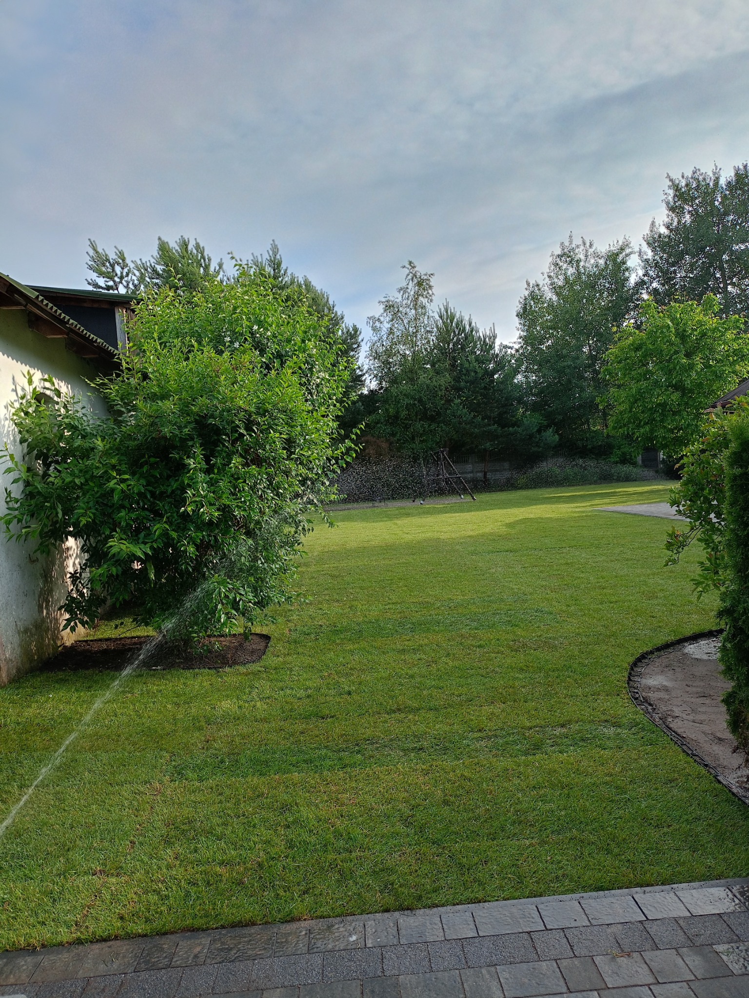 Nawadnianie trawnika z rolki przy ścianie budynku, widoczny fragment systemu nawadniania.