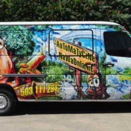 Biały van z kolorową, humorystyczną grafiką reklamową, zawierającą postać kobiety, logo firmy i numer telefonu, zaparkowany na zewnątrz.