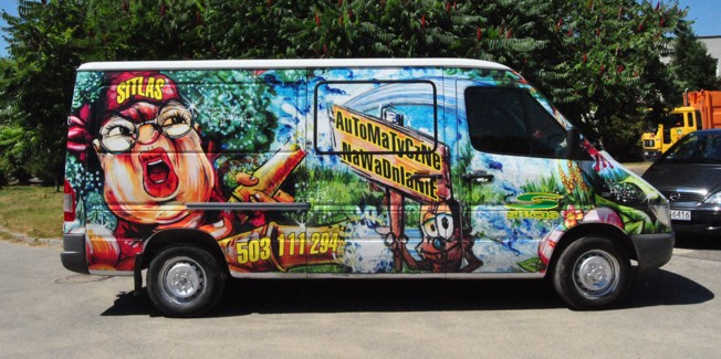 Biały van z kolorową, humorystyczną grafiką reklamową, zawierającą postać kobiety, logo firmy i numer telefonu, zaparkowany na zewnątrz.