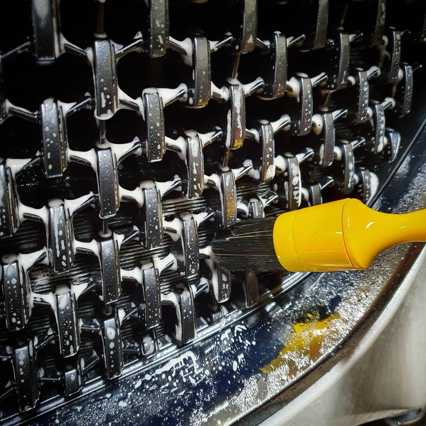 Szczoteczka z żółtą rączką czyści chromowany grill samochodu pokryty pianą.