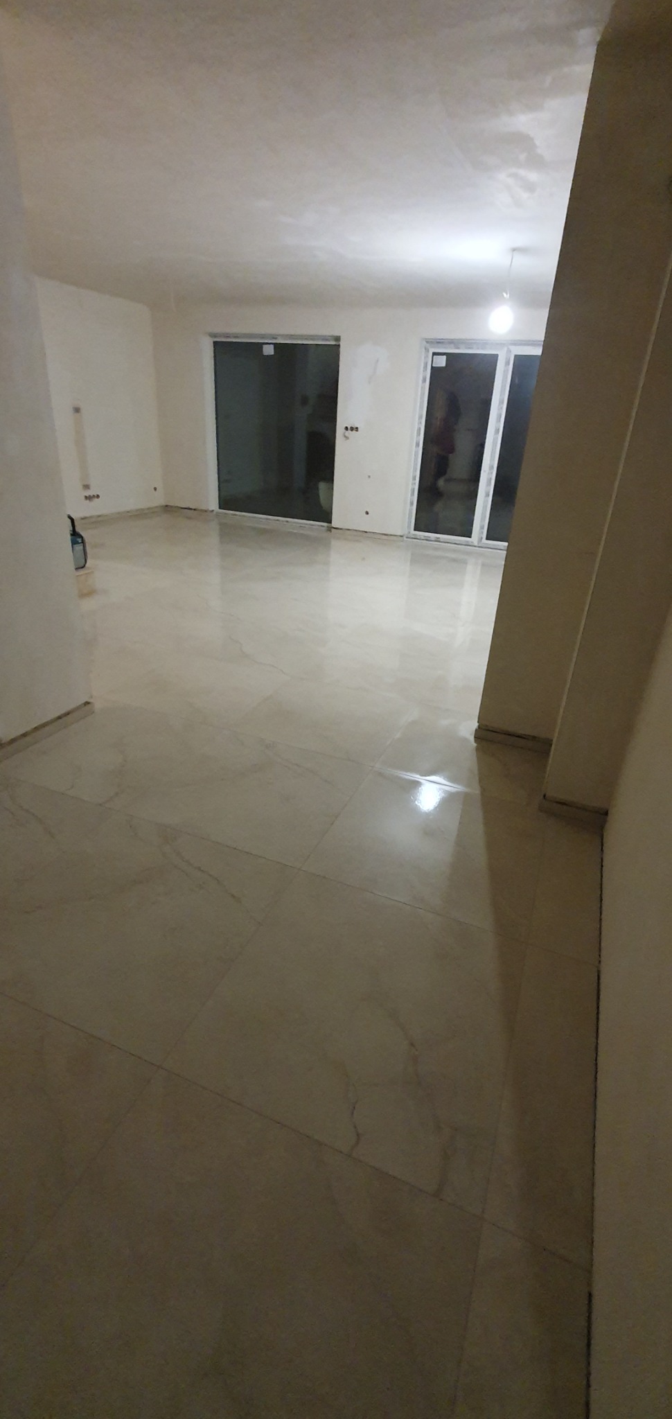 Wykończone wnętrze z błyszczącą, beżową podłogą z płytek imitujących marmur, duże przesuwne okna balkonowe i świeżo pomalowane ściany na biało.