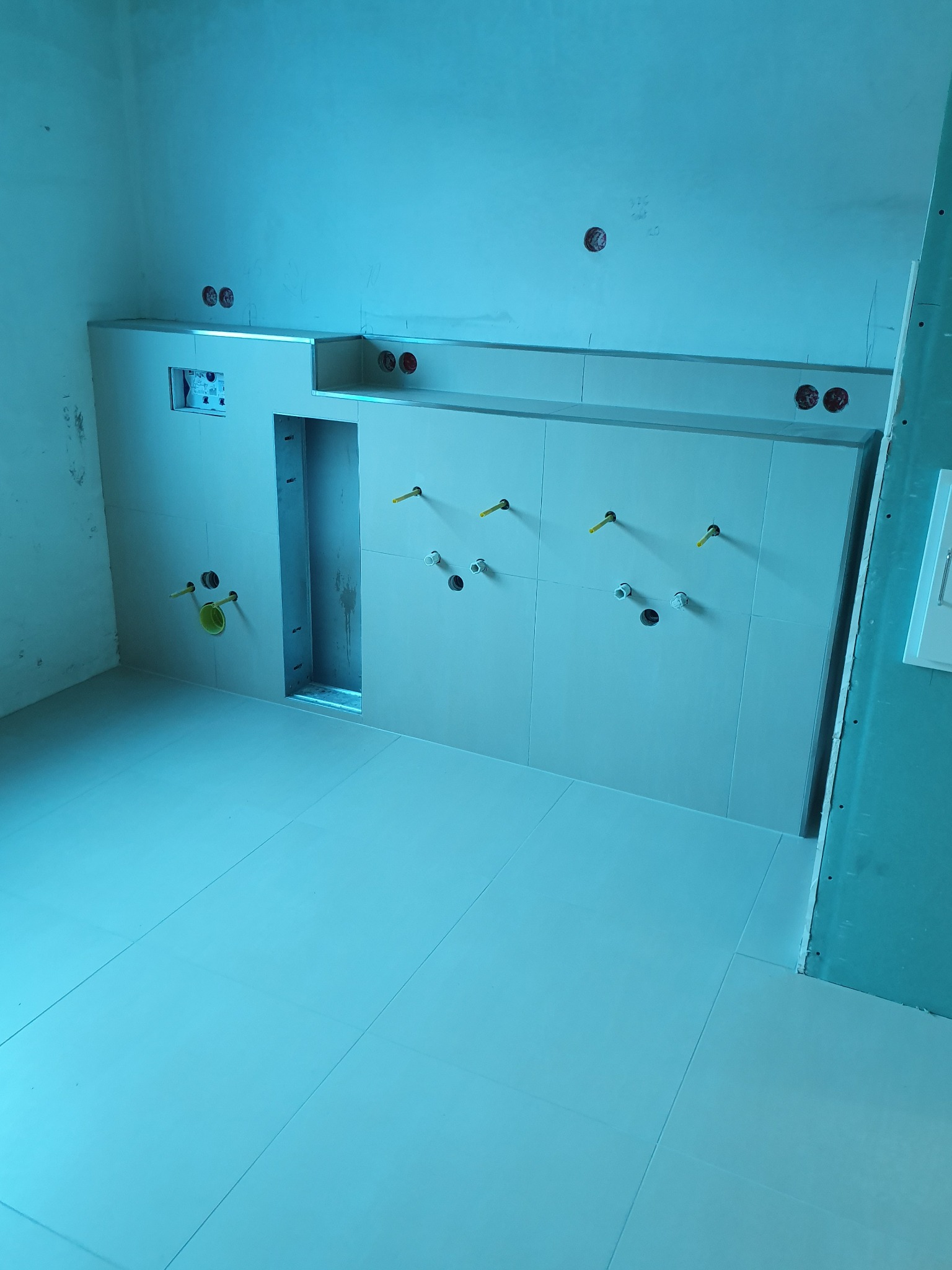 Łazienka w trakcie remontu: ułożone jasne płytki podłogowe i ścienne, widoczne wystające rury i otwory na armaturę, ściany w surowym stanie.