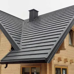 Nowy, grafitowy dach z blachodachówki modułowej na drewnianym domu, widok z dołu, rynna w kolorze dachu.
