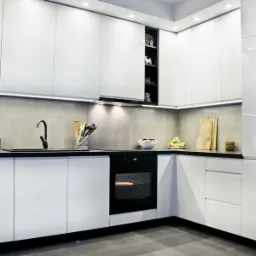 Nowoczesna, minimalistyczna kuchnia z białymi, lakierowanymi frontami, czarnym blatem i szarymi płytkami na ścianie, oświetlenie LED podszafkowe, piekarnik w zabudowie i akcesoria kuchenne na blacie.