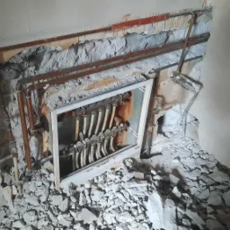 Rozdzielacz centralnego ogrzewania wnękowy, widoczne rury miedziane, biała rama, gruz po kuciu w ścianie.