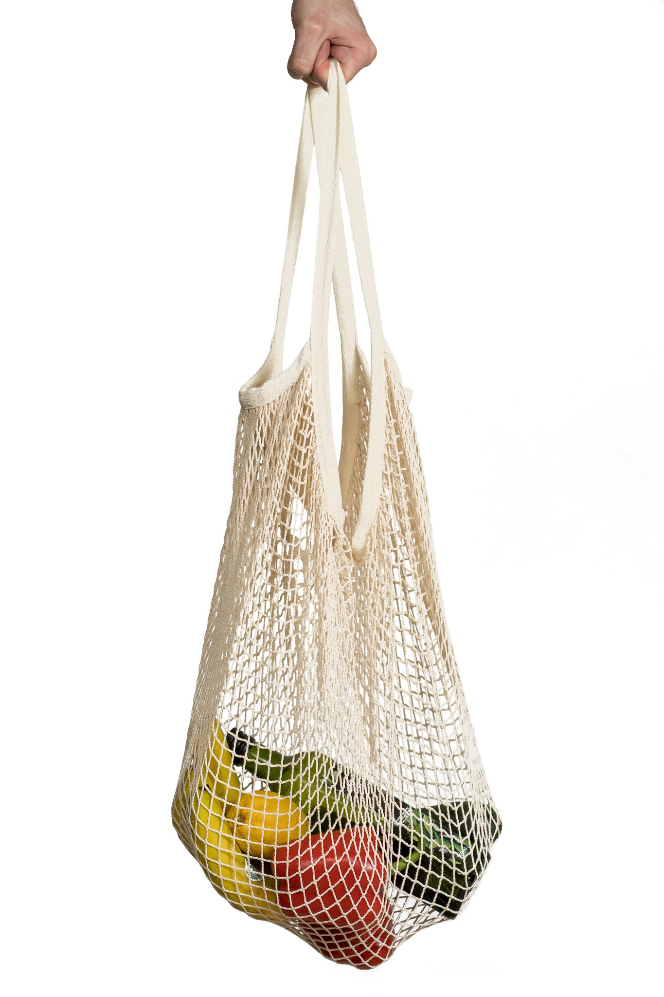 Ręka trzyma beżową siatkową torbę na zakupy z widocznymi w środku bananami, czerwoną papryką i zielonym awokado na białym tle.