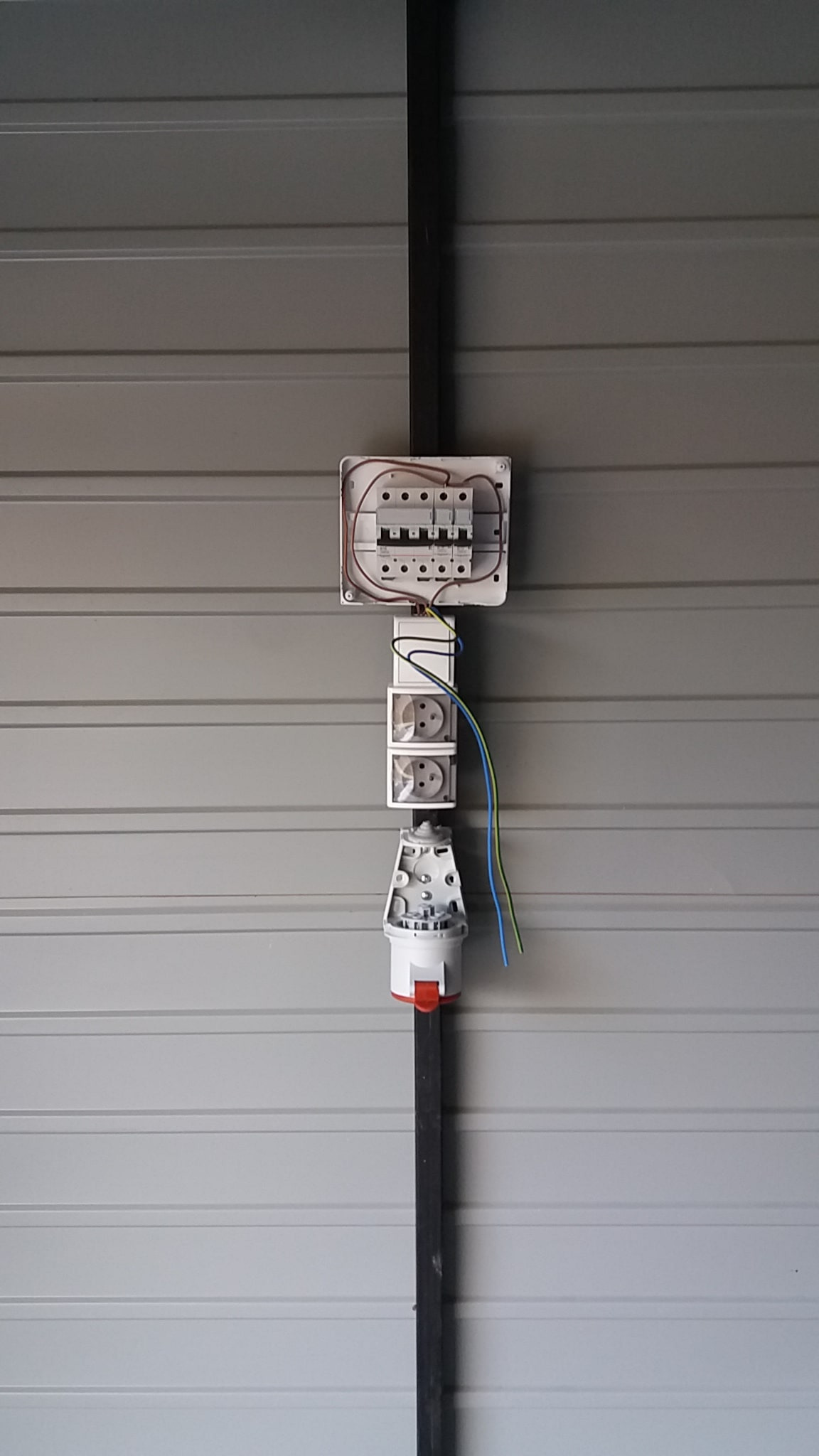 Rozdzielnica elektryczna z bezpiecznikami, gniazda przemysłowe i wtyczka zamontowane na ścianie z blachy trapezowej.