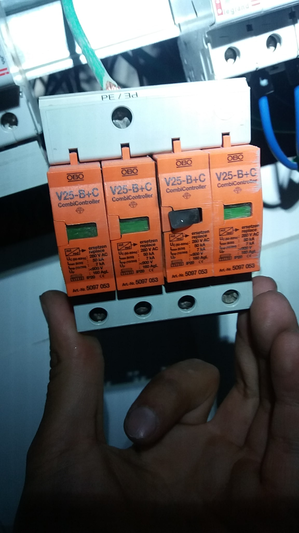 Pomarańczowe ograniczniki przepięć OBO V25-B+C CombiController, z jednym przełącznikiem w pozycji wyłączonej, zamontowane na szynie, trzymane w dłoni.