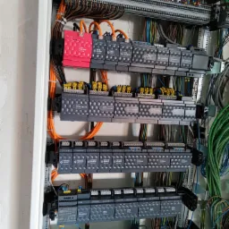 Rozdzielnica elektryczna z modułami sterującymi Grenton, widoczne liczne przewody i złączki, obudowa w kolorze białym.