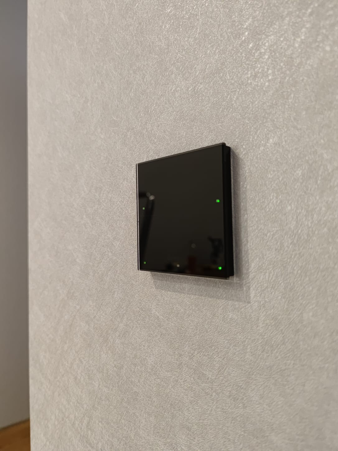 Czarny, dotykowy panel sterowania klimatyzacją z zielonymi diodami LED zamontowany na szarej ścianie o teksturowanej powierzchni.