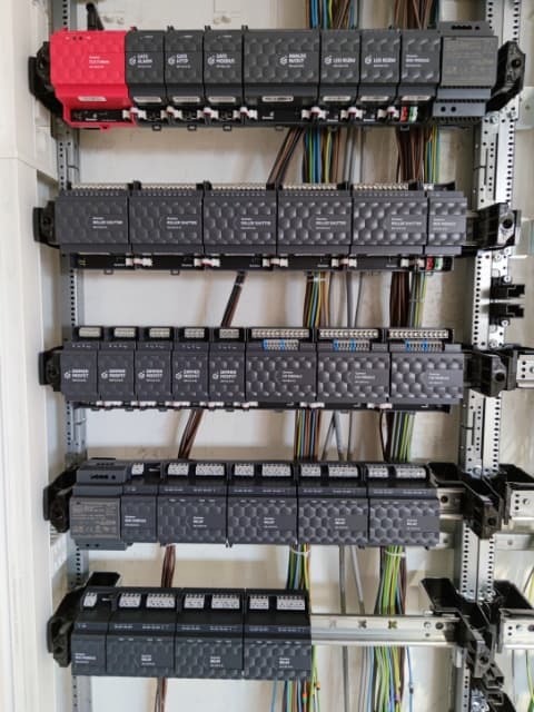 Rozdzielnica elektryczna z modułami sterującymi, widoczne okablowanie i elementy montażowe na szynie DIN.