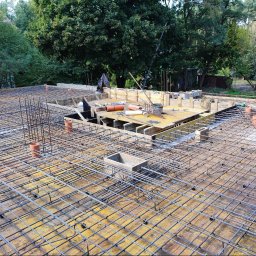 WM Your Home Waldemar Majek - Zbrojenie stropu budynku jednorodzinnego z widocznymi elementami szalunków i instalacji, przygotowane do zalania betonem. Widok z góry na tle zieleni.