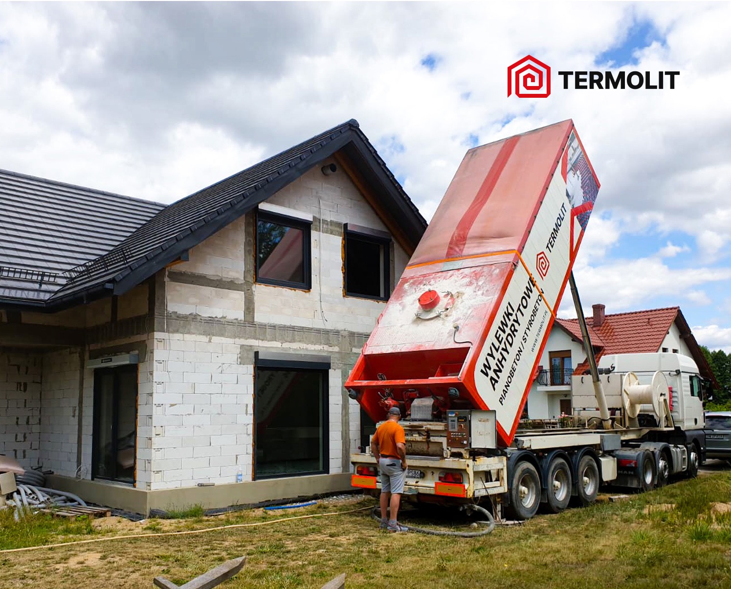 Ciężarówka z podnośnikiem do wylewek anhydrytowych marki Termolit przy budynku w stanie surowym zamkniętym, widoczny pracownik obsługujący maszynę.