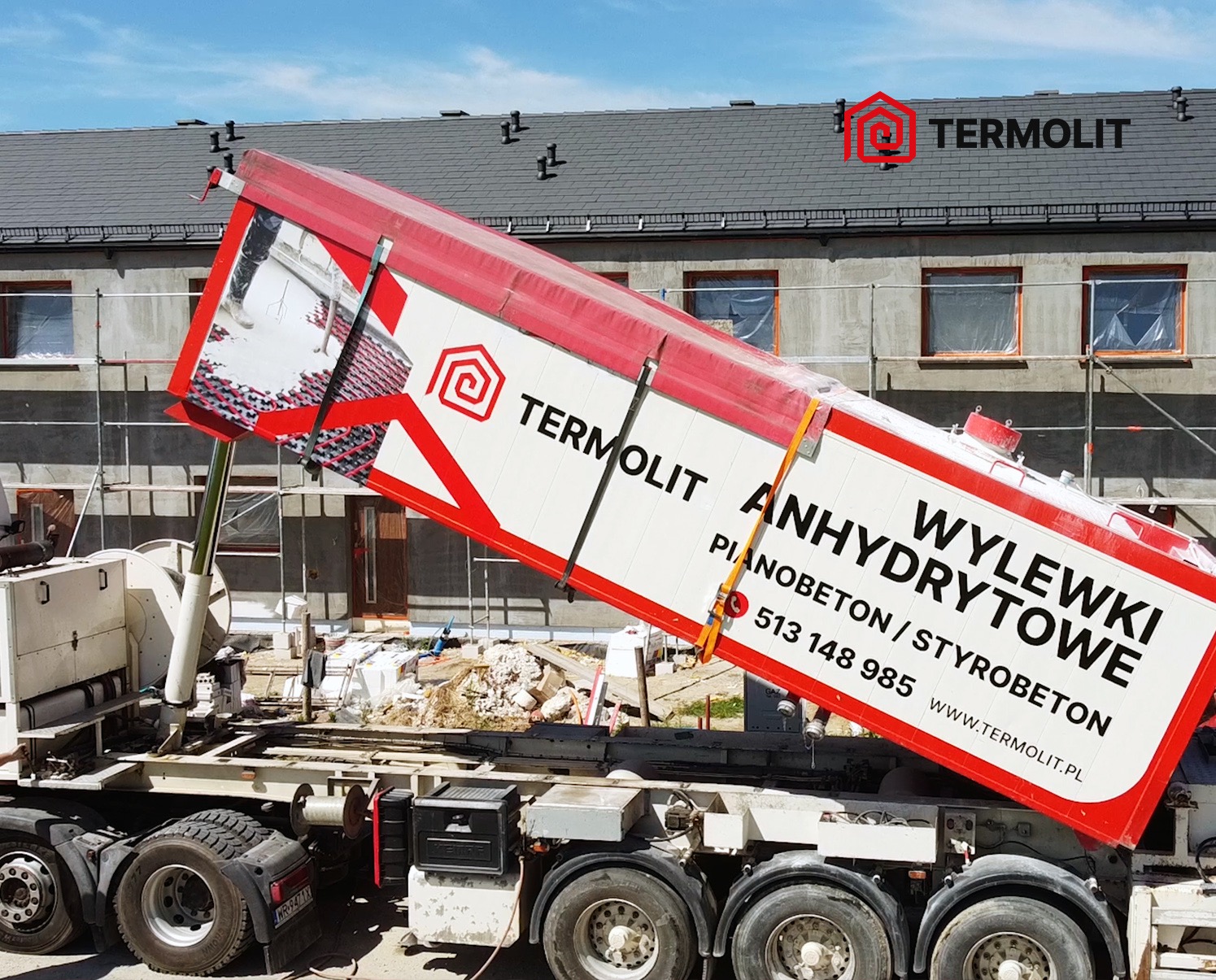 Ciężarówka z podniesioną skrzynią ładunkową z napisem 'Wylewki Anhydrytowe' firmy z Wrocławia, na tle budynku w trakcie prac wykończeniowych.