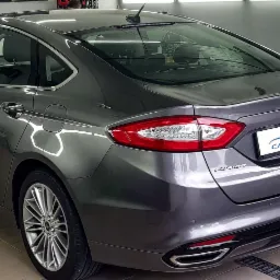 Błyszczący, szary Ford Fusion po usłudze mycia, widoczny z tyłu, z logo Cars Spa na karoserii i odbiciami światła na lakierze.