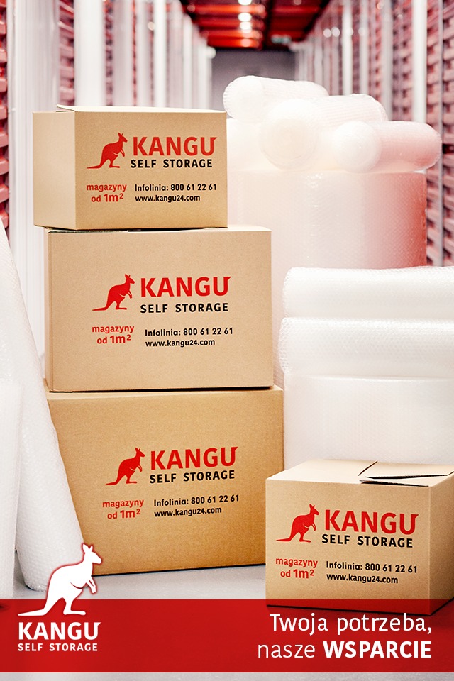 Stos kartonowych pudeł z logo firmy Kangu Self Storage, obok rolki folii bąbelkowej i folii stretch, w tle regały magazynowe.
