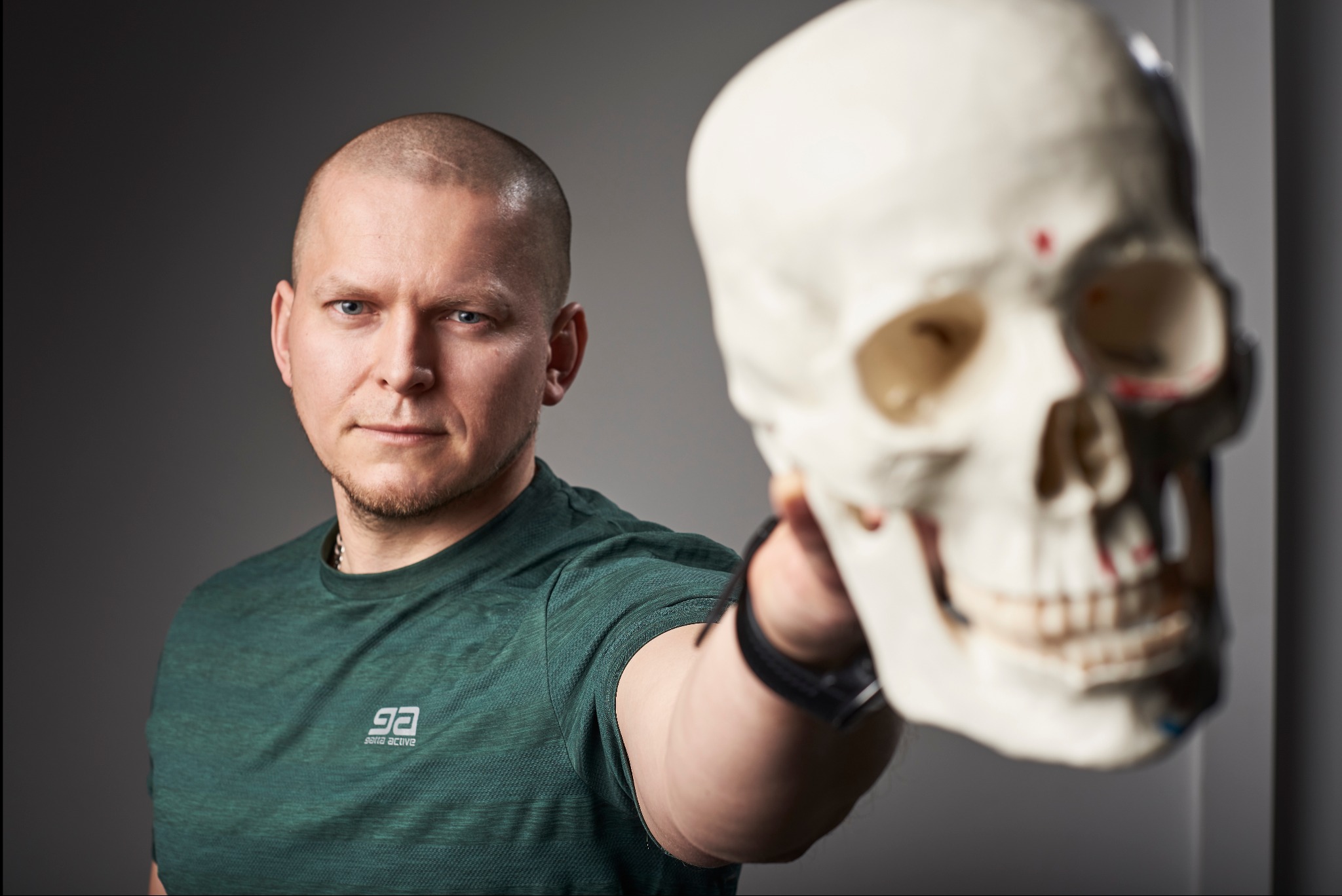 Mężczyzna w zielonej koszulce trzyma model czaszki ludzkiej, prezentacja anatomii.