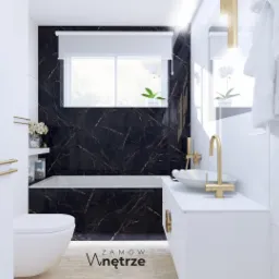 Elegancka łazienka z czarnymi płytkami imitującymi marmur, złotą armaturą i białymi meblami. Widoczne WC, wanna, umywalka nablatowa, grzejnik drabinkowy i dekoracje, takie jak storczyk w doniczce.