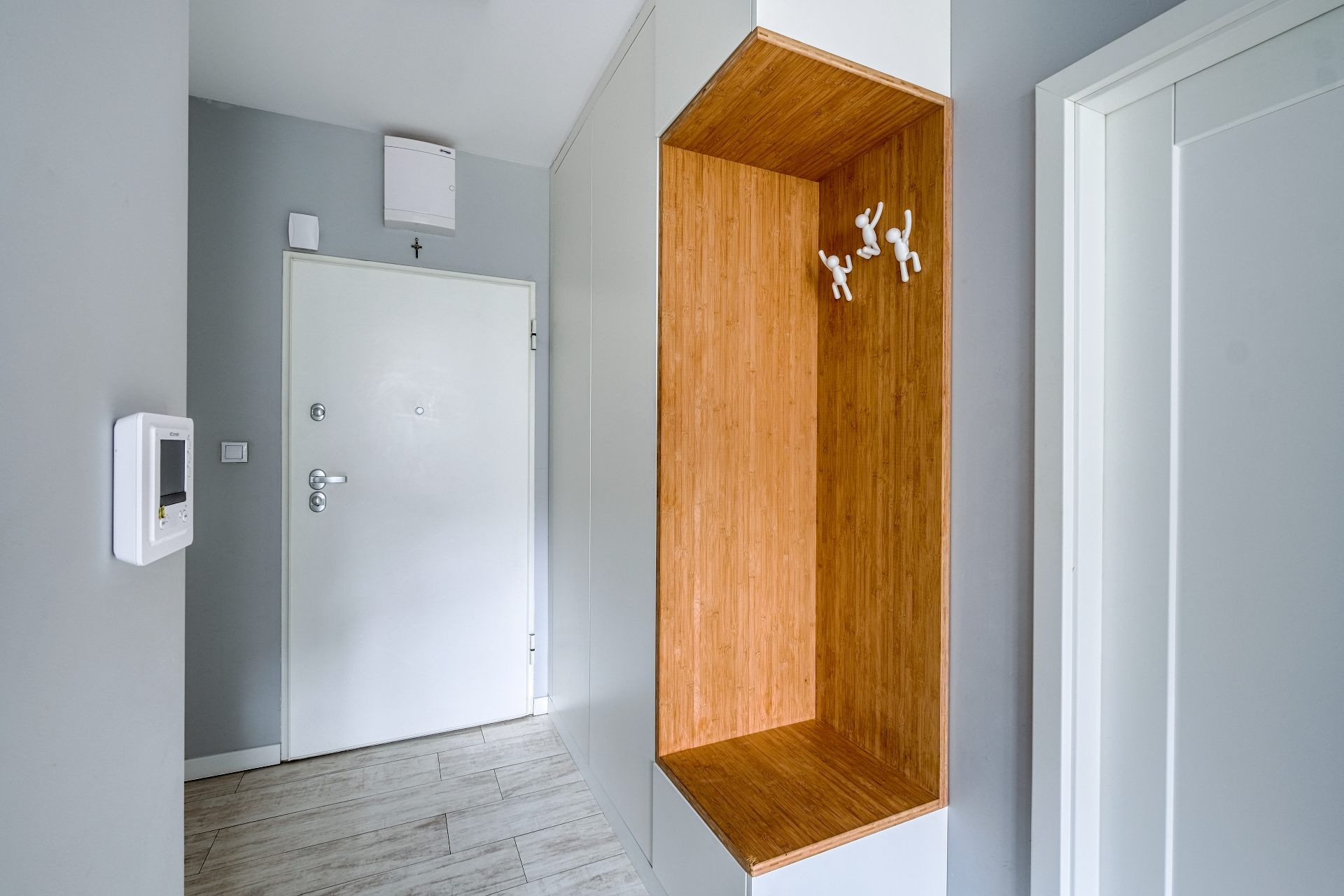 Nowoczesny przedpokój z białą szafą w zabudowie i wnęką z bambusowym wykończeniem, na której umieszczono designerskie wieszaki w kształcie ludzików.